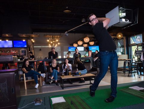 Man plays indoor golf while friends watch